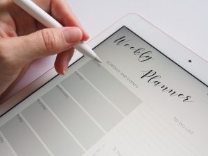A tablet with a weekly planner on the screen and a hand with a writing stylus.